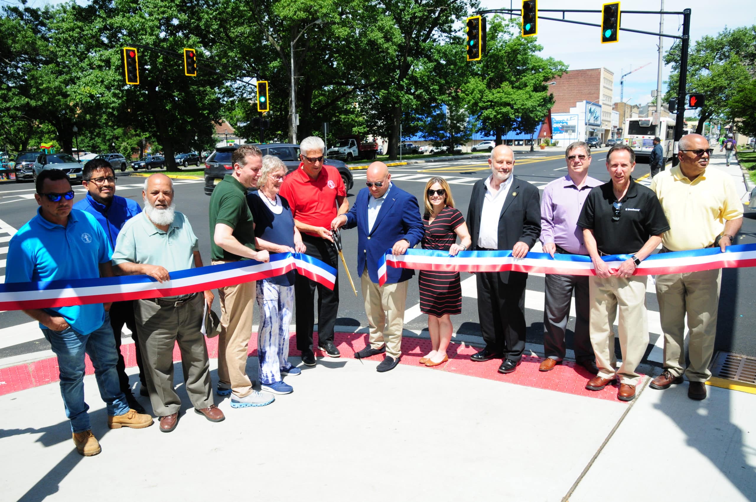 A sunny day with with 11 people standing behind a ribbon being cut at a Bloomfield Ave. intersection.