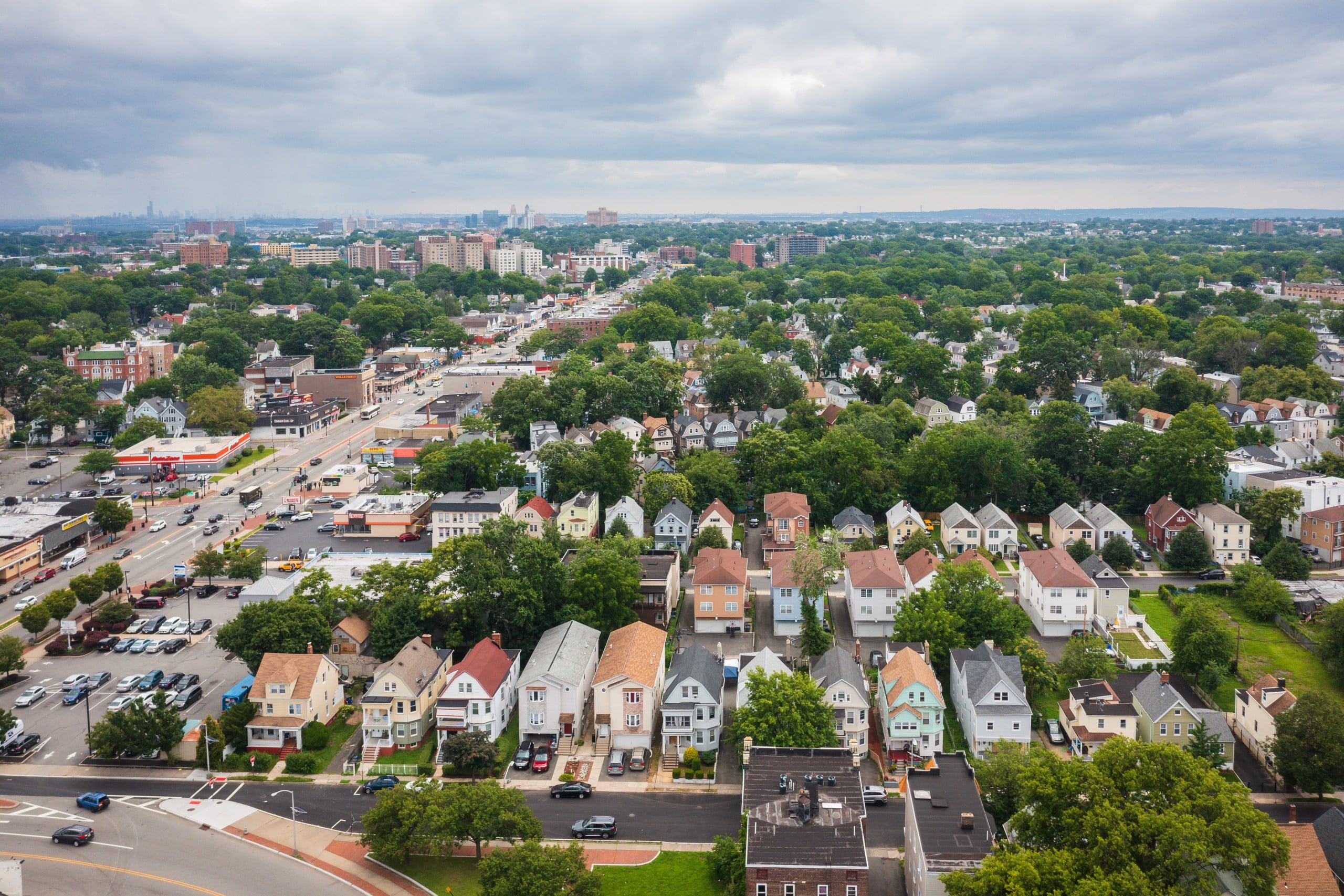 An aerial view of Essex County with houses and businesses near East Orange's Central Ave. in the foreground and Newark and New York City in the distance.