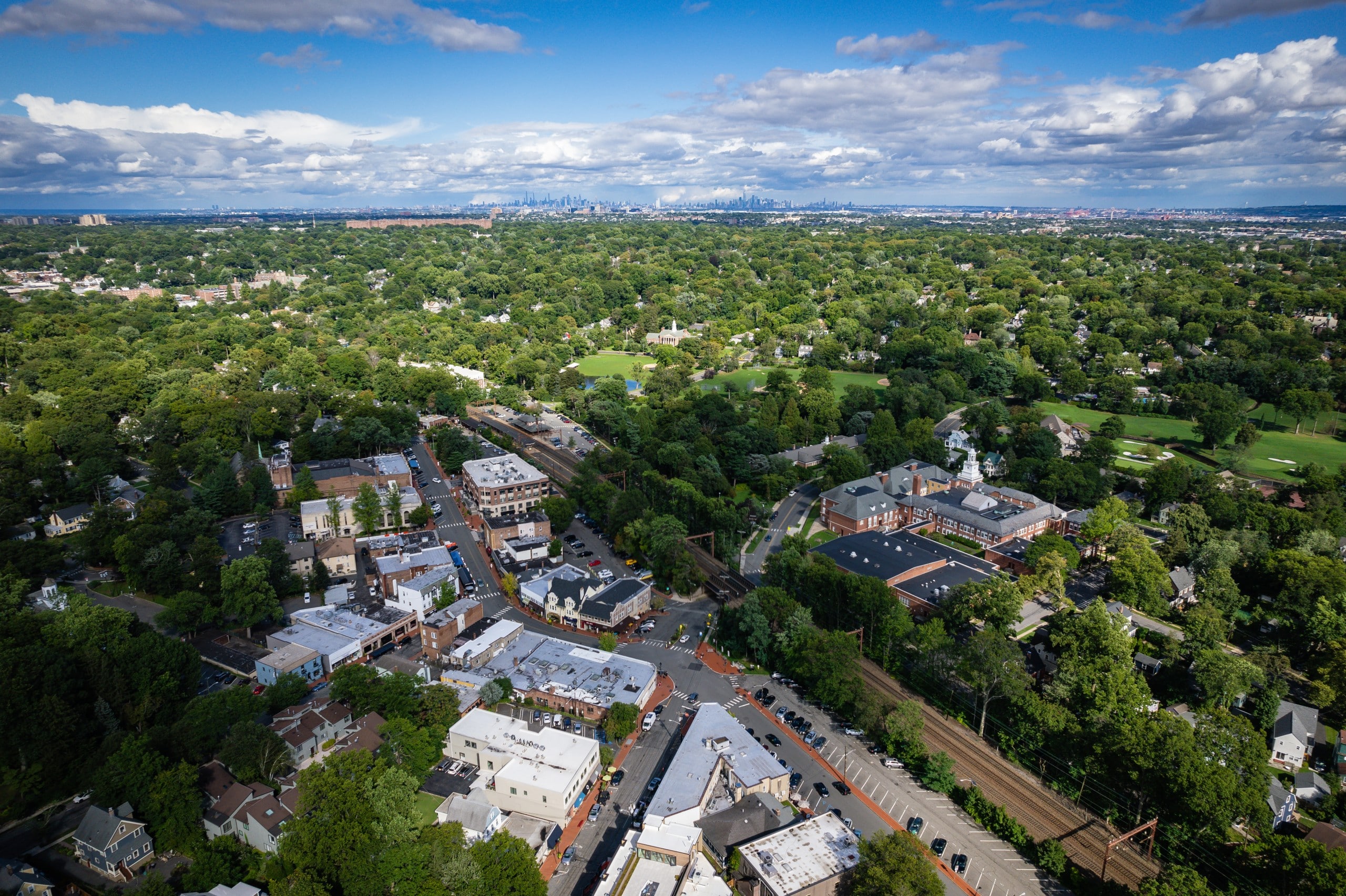 An aerial view of Maplewood, NJ looking towards New York City with Newark, the Oranges, and other East Essex County communities in the background.