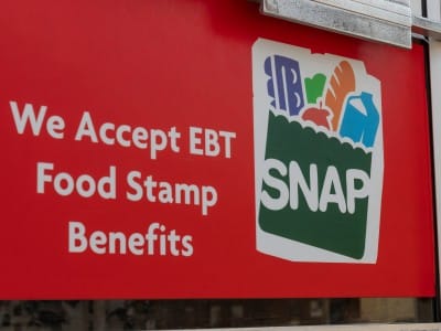 A red sign on the outside of store door reads "We accept EBT food stamp benefits."