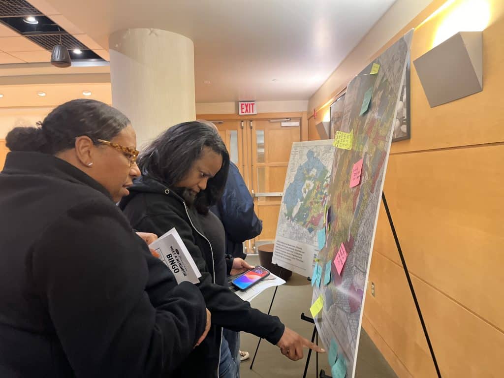 Two women standing in front of a 1930s federal map of Essex County reviewing Post-It note observations of the map left by segregation and reparation forum attendees.