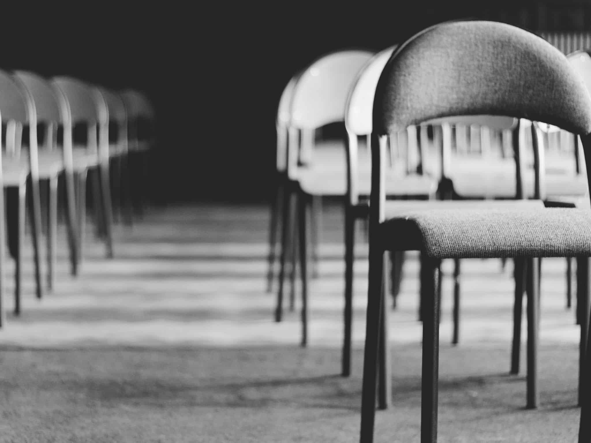 Black and white photo showing rows of empty chairs arranged in a spacious indoor setting.